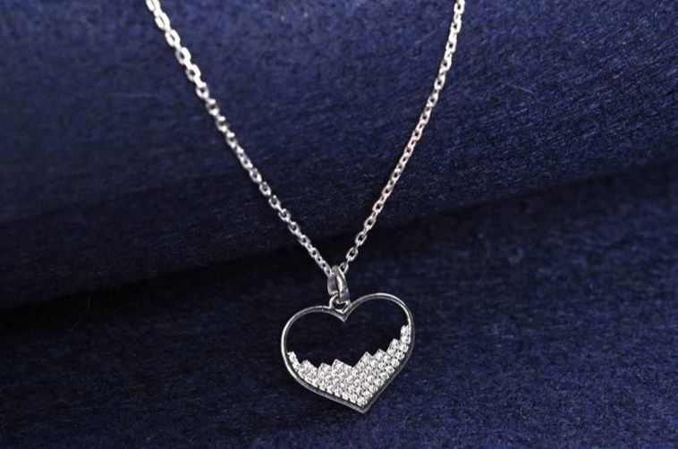Silver heart pendant necklace displayed on dark blue fabric background