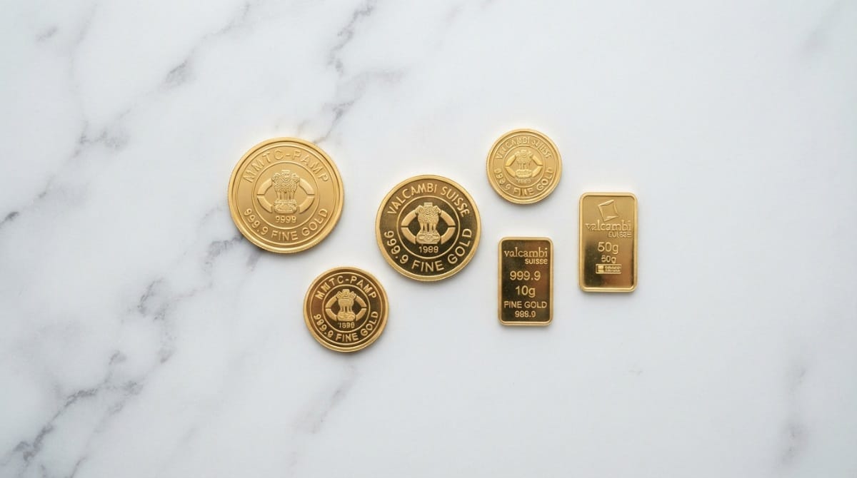 Gold coins and a gold bar with fineness marks arranged on a clean white surface
